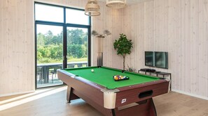 A pool table with balls, a television, and a plant in a room with large windows and wooden walls.