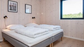 A double bed with white bedding, two wall-mounted lamps, and a window with a view of greenery.