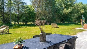An outdoor patio with a table and chairs, surrounded by a grassy area and trees.