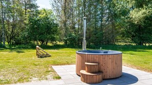 Banyera d'hidromassatge amb escales de fusta i un tub metàl·lic en una zona enjardinada amb arbres.