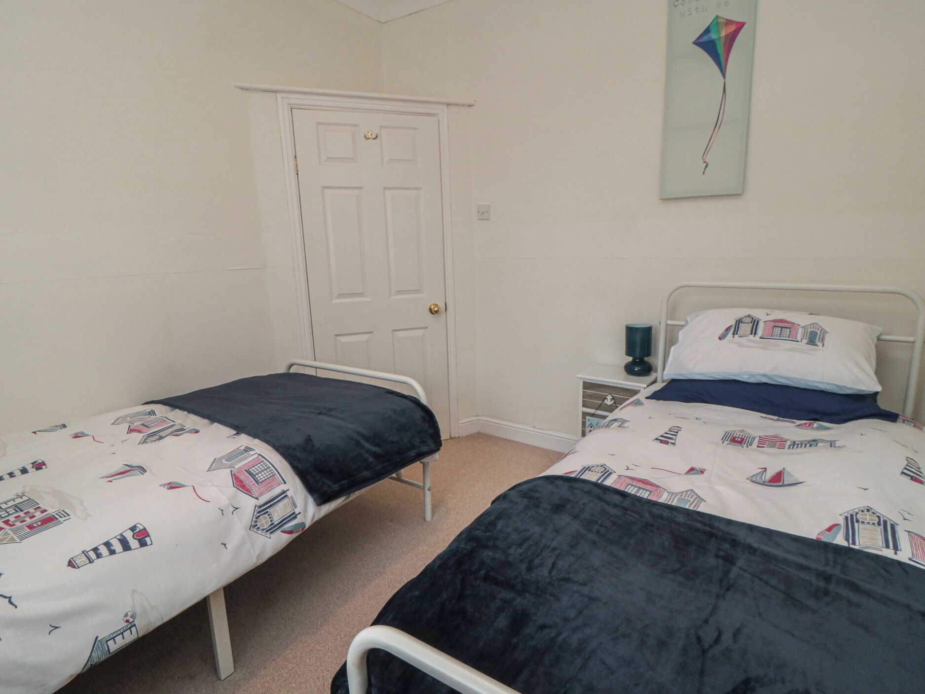 A small, simple room with two single beds, a door, a nightstand, and a wall-mounted kite decoration.