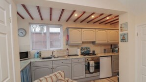 A compact kitchen with wooden beams, a dining area with striped furniture, and a clock on the wall. - Seabreeze (Filey)
