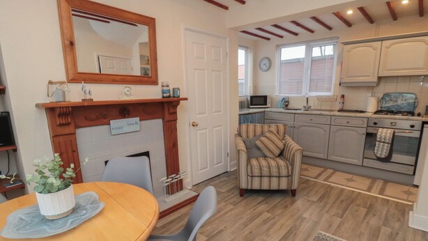A cozy kitchen with a wooden dining table, a comfortable armchair, and a fireplace. - Seabreeze (Filey)