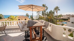 A wooden table with a beige umbrella, surrounded by cushioned chairs, on a balcony with a view of the ocean and palm trees. - CostaBlancaDreams - Villa Vista in Calpe (Calpe)