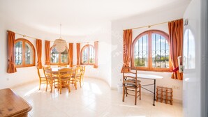 A spacious dining area with a round table and chairs, large arched windows with curtains, and a hanging light fixture. - CostaBlancaDreams - Villa Vista in Calpe (Calpe)