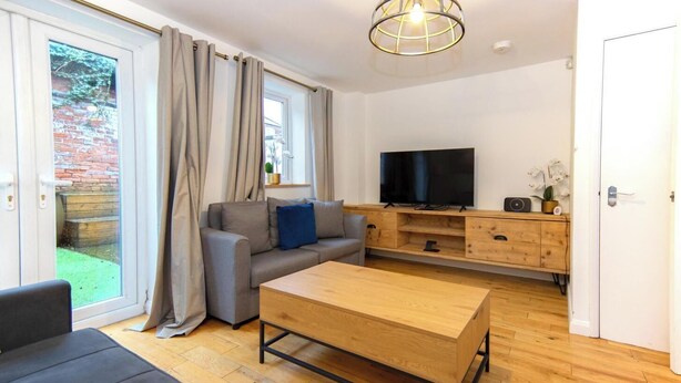 A modern living room with a grey sofa, a wooden coffee table, and a TV on a wooden stand. - Stylish Town House - Located close to Derby centre (Derby)