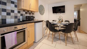 A modern kitchen with wooden cabinets, a black countertop, and a dining area with a round table and chairs. - Stylish Town House - Located close to Derby centre (Derby)
