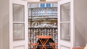 Una habitación con una puerta blanca que da a un balcón con barandilla de hierro forjado y una pequeña mesa.
