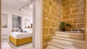 Un dormitorio con cama, ventana con cortinas, mesita de noche y una planta en maceta sobre una escalera.