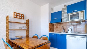 A compact kitchen with blue cabinets, a wooden dining table, and a white dishwasher. - Apartment for 6, sea view terrace, Wi-Fi (Roquebrune-Cap-Martin)