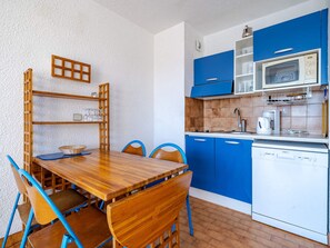 A compact kitchen with blue cabinets, a wooden dining table, and a white dishwasher. - Apartment for 6, sea view terrace, Wi-Fi (Roquebrune-Cap-Martin)