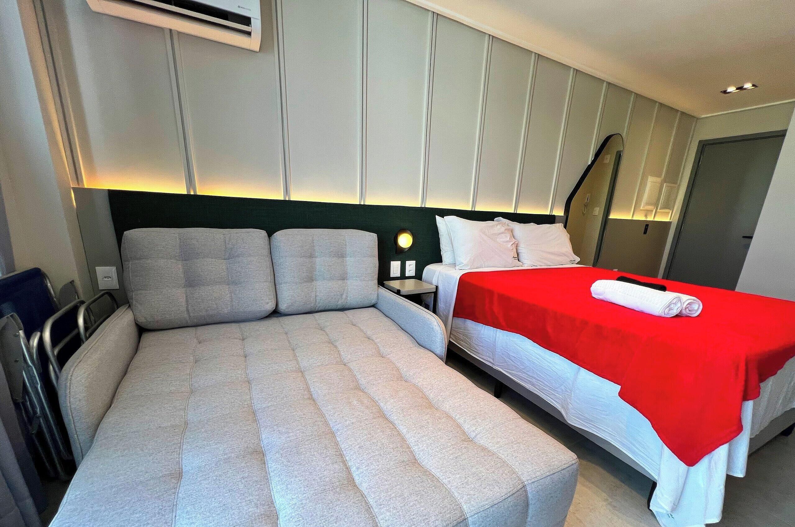 A hotel room with a bed, a seating area, a nightstand, and a mirror.