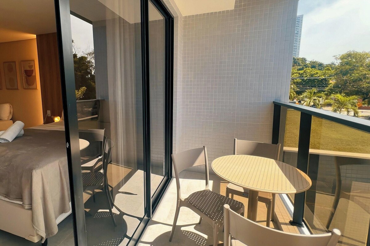 Una habitación de hotel moderna con una cama, un balcón con mesa y sillas, y vistas al exterior.