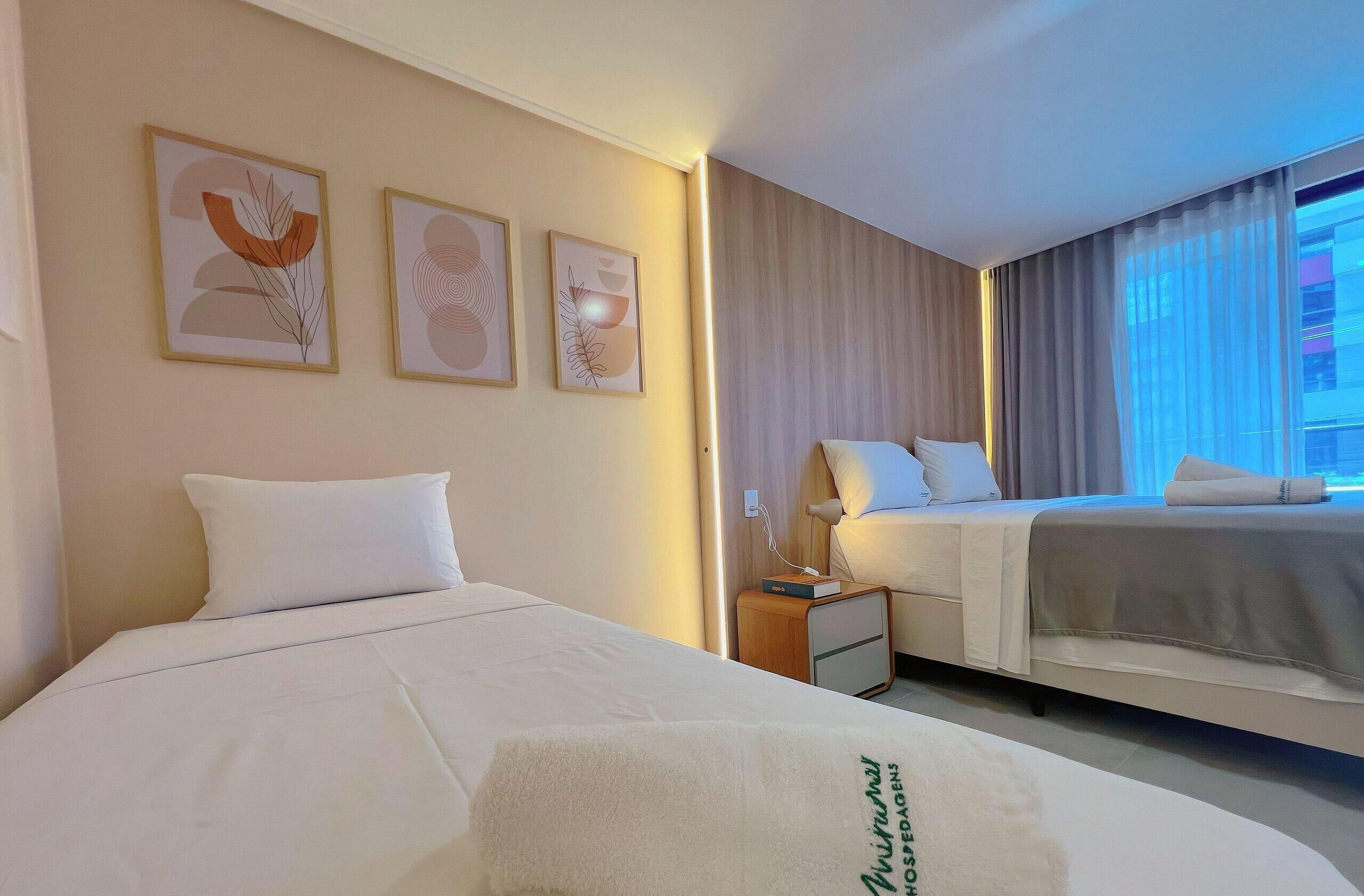 A hotel room with two beds, a nightstand, a lamp, and wall art.