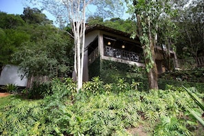 Un bâtiment doté d’un balcon, entouré d’une végétation luxuriante et d’arbres.