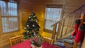 A wooden cabin interior with a Christmas tree, a dining table with a red tablecloth, and a staircase with red stockings. - Lakeview Cabin w/ Loft • Grill • Resort Amenities (Columbia)