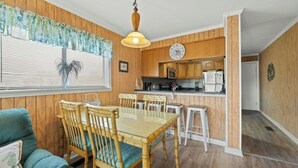 Un comedor con mesa y sillas de madera, una cocina con armarios y electrodomésticos de madera, y un ventanal con persianas.