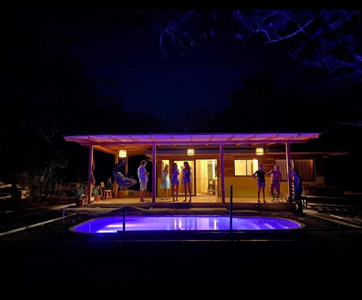 A covered outdoor area with a pool, a wooden structure, and a group of people standing around.