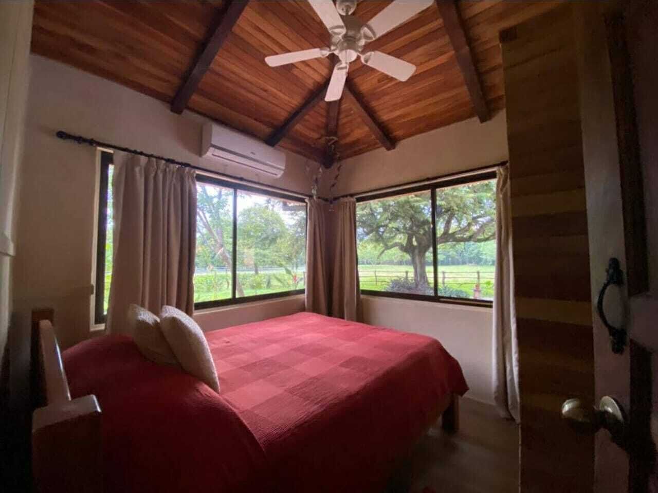 Une chambre à coucher avec un lit, un ventilateur de plafond, de grandes fenêtres et un appareil de climatisation.