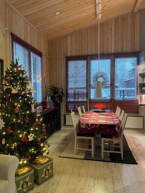 Un coin repas chaleureux avec un plafond en bois, un sapin de Noël et une table dressée pour quatre personnes.