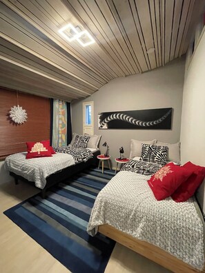 Une chambre moderne avec deux lits, un tapis à rayures et un luminaire suspendu au plafond.