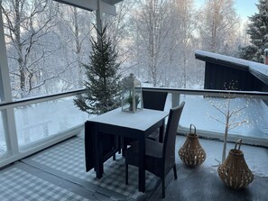 Un balcon avec un sol à carreaux, une table avec des chaises, un petit sapin de Noël et deux lanternes en osier.