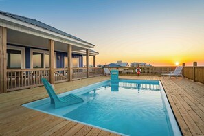 A pool area with a wooden deck, lounge chairs, and a building with a covered deck.