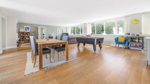 Een ruime woonruimte met een pooltafel, een eettafel met stoelen, een bank en een boekenkast.