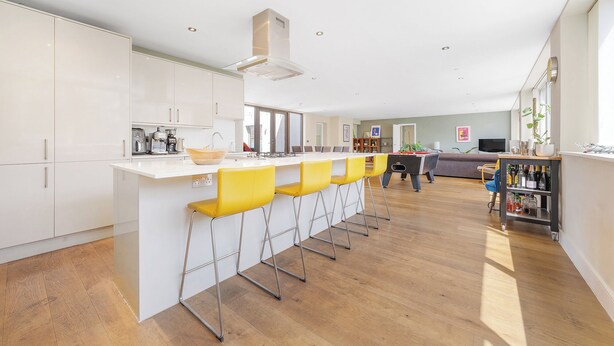Een moderne keuken met een centraal eiland, barkrukken en een zithoek met een bank en salontafel.