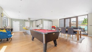 Een moderne woonkamer met een pooltafel, een blauwe bank en een eethoek met stoelen en een tafel.