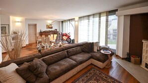 Een moderne woonkamer met een grote, bruine modulaire bank, een eethoek met een houten tafel en stoelen, en een motorfiets op de achtergrond.