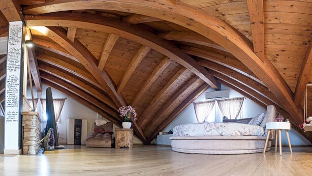 Een ruime zolderkamer met houten balken, een ronde bank en een kleine tafel.