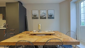 A dining area with a large wooden table, metal chairs, and a candle centerpiece. There are three framed artworks on the wall above the table. - Relaxing 2-Bed Apartment near Tooting Bec & Balham - Pass the Keys (London)