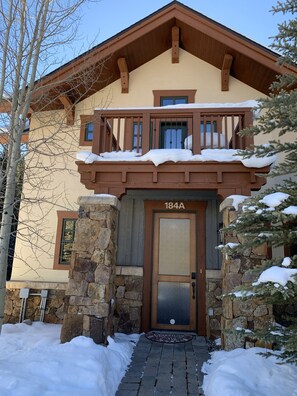 A two-story house with a stone facade, a wooden balcony, and a snow-covered roof. - Custom 4BR/4BA ski-in townhome, private hot tub at Copper Mountain, 184A (Copper Mountain)