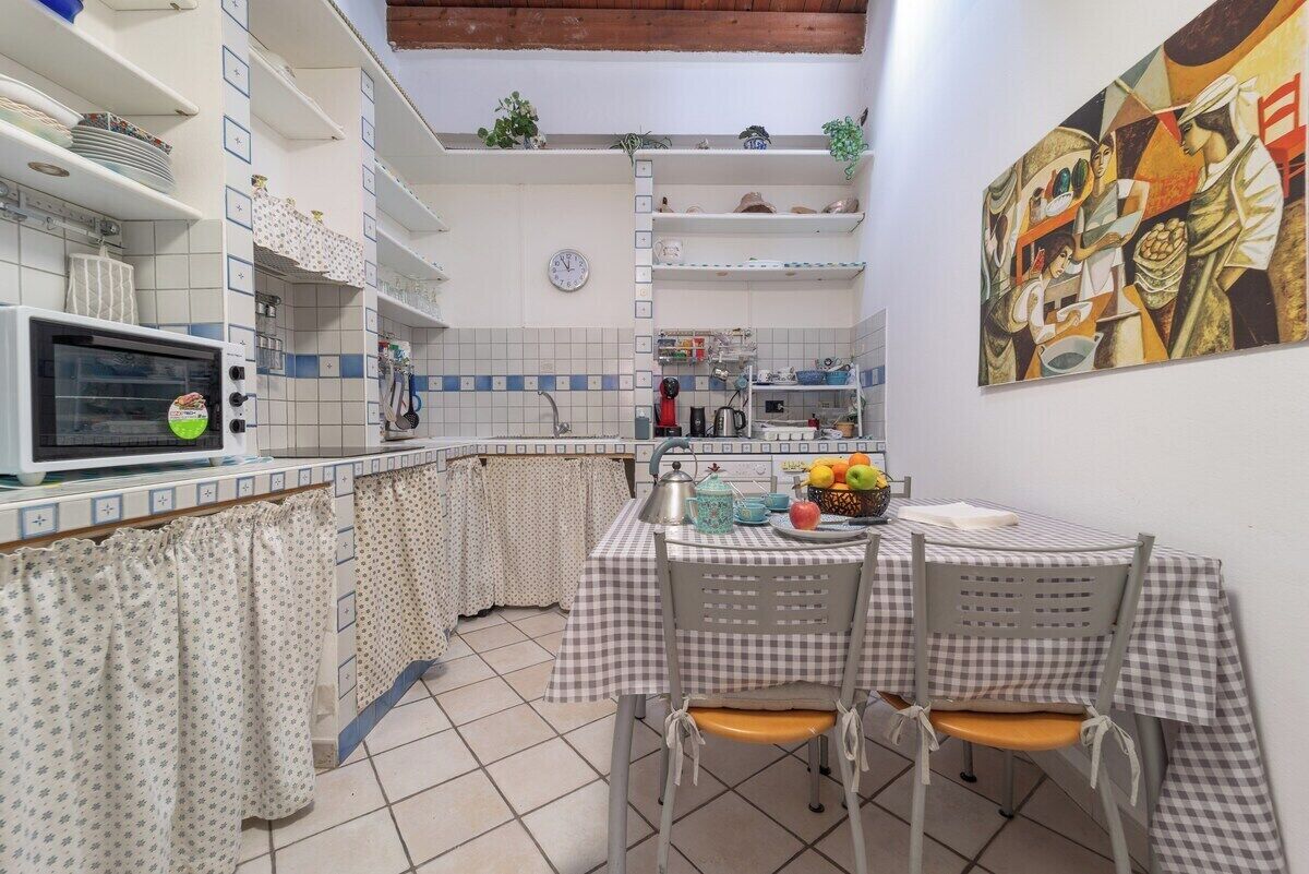 A compact kitchen with a microwave, a kettle, and a table set for two with chairs.