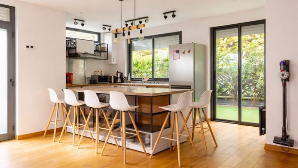 Cozinha moderna com ilha central, banquetas de bar e uma ampla janela com vista para o verde.