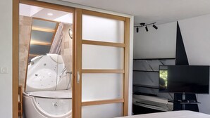 Um quarto com uma cama grande, televisão, banheira e um guarda-roupa de madeira.