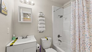 Ein Badezimmer mit Waschbecken, Toilette und Dusche. Über dem Spiegel befinden sich Lampen und ein Handtuchhalter mit Handtüchern.