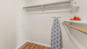 Ein Blick in einen Raum mit Holzboden, weißen Wänden und einer weißen Decke. Man sieht einen weißen Haken mit einem gemusterten Handtuch, eine Holzablage mit einem Paar orangener Schuhe und einen weißen Vorhang mit Blumenmuster.