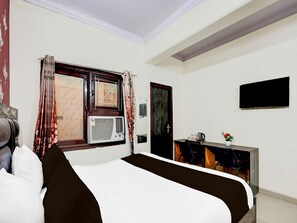 A hotel room with a bed, a desk with a chair, a television mounted on the wall, and a window with curtains. - Collection O Nehru Nagar (Ghaziabad)