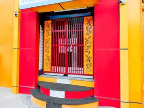 A brightly colored building with a red and yellow facade, a barred entrance, and a small set of steps leading up to the door. - Collection O Nehru Nagar (Ghaziabad)