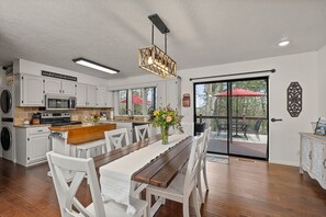A kitchen with white cabinets, a wooden dining table, and a large window.
