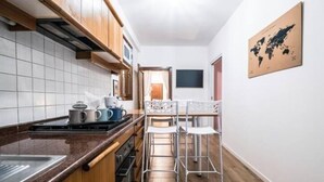 Eine Küche mit Holzausstattung, einer Fliesenküchenwand und einem Edelstahl-Spülbecken. Zwei weiße Barhocker und ein kleiner Tisch mit einer Weltkarte an der Wand.