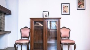 Eine Holzvitrine mit Glastüren, zwei Polsterstühle und gerahmte Bilder an der Wand.