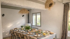 A dining area with a long table set for a meal, surrounded by wicker chairs, with a rustic ceiling and a window providing natural light. - La Villa Bellerose is a cosy Zen gîte on the Côte d'Opale, near Le Touquet. (Beutin)