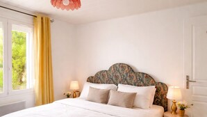 A bedroom with a large bed, two bedside tables with lamps, a patterned headboard, and a view of greenery through a window. - La Villa Bellerose is a cosy Zen gîte on the Côte d'Opale, near Le Touquet. (Beutin)
