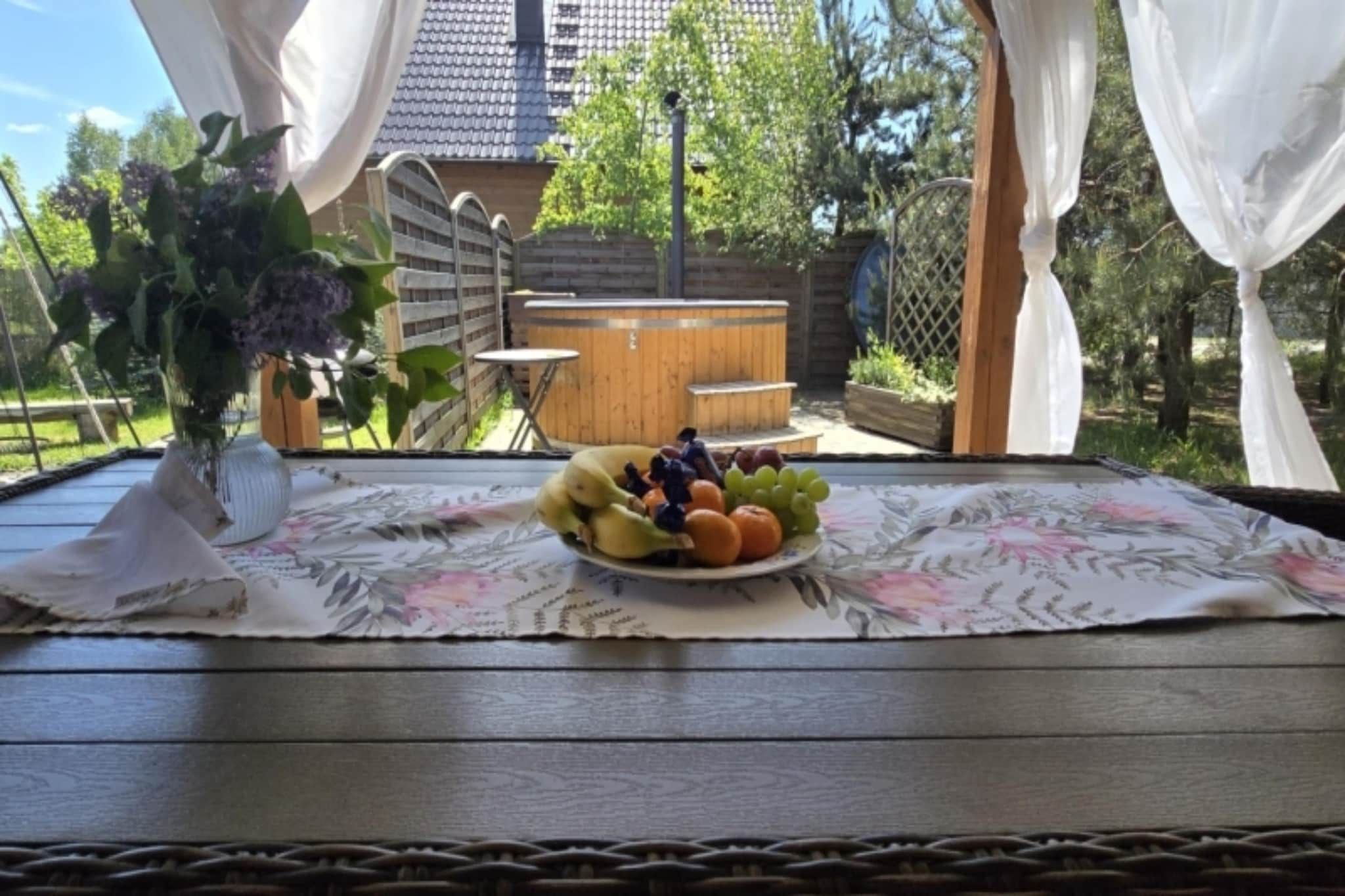 Una mesa con mantel floral, un plato de fruta y un jarrón blanco con flores.