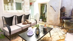 Eine Terrasse mit bequemen Sitzgelegenheiten, einem Tisch mit Flasche und Gläsern sowie Kübelpflanzen.