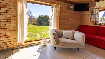 Ett rum med ett stort fönster, en röd soffa, en beige fåtölj och ett litet bord med en dekorativ prydnad.