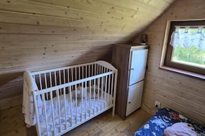 A wooden room with a crib, a small cabinet, and a window with a view of greenery. - Holiday home, private sauna and jacuzzi (Balachy)